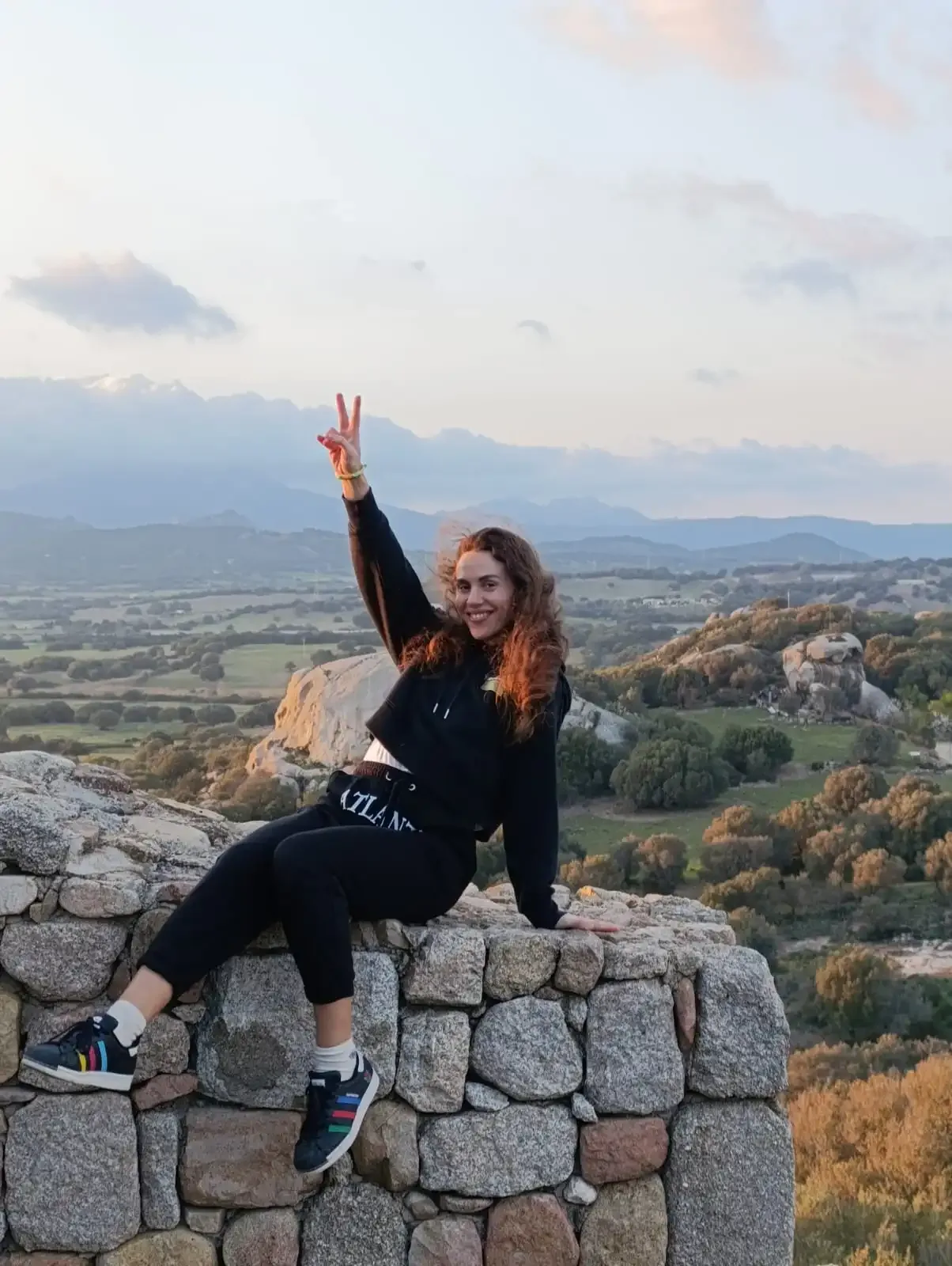 Frau auf einer Steinmauer zeigt das Peace-Zeichen