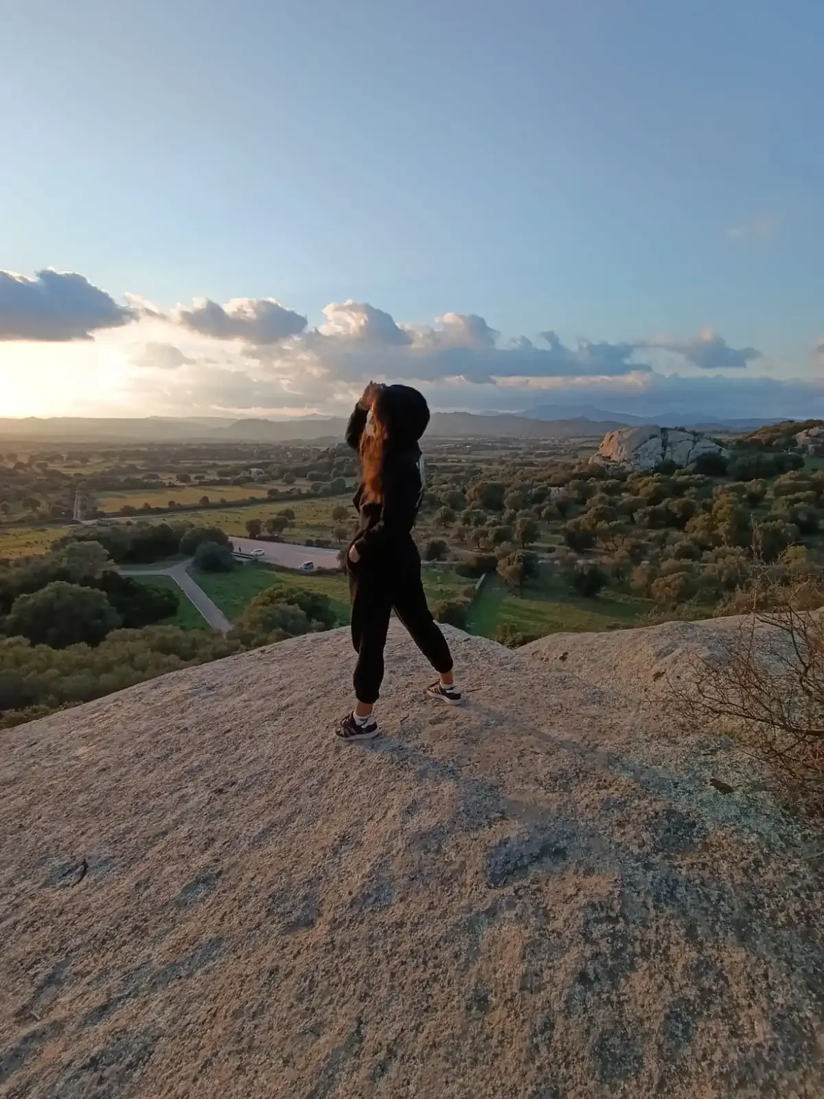 Frau auf einem Felsen betrachtet die Sonnenuntergangslandschaft.
