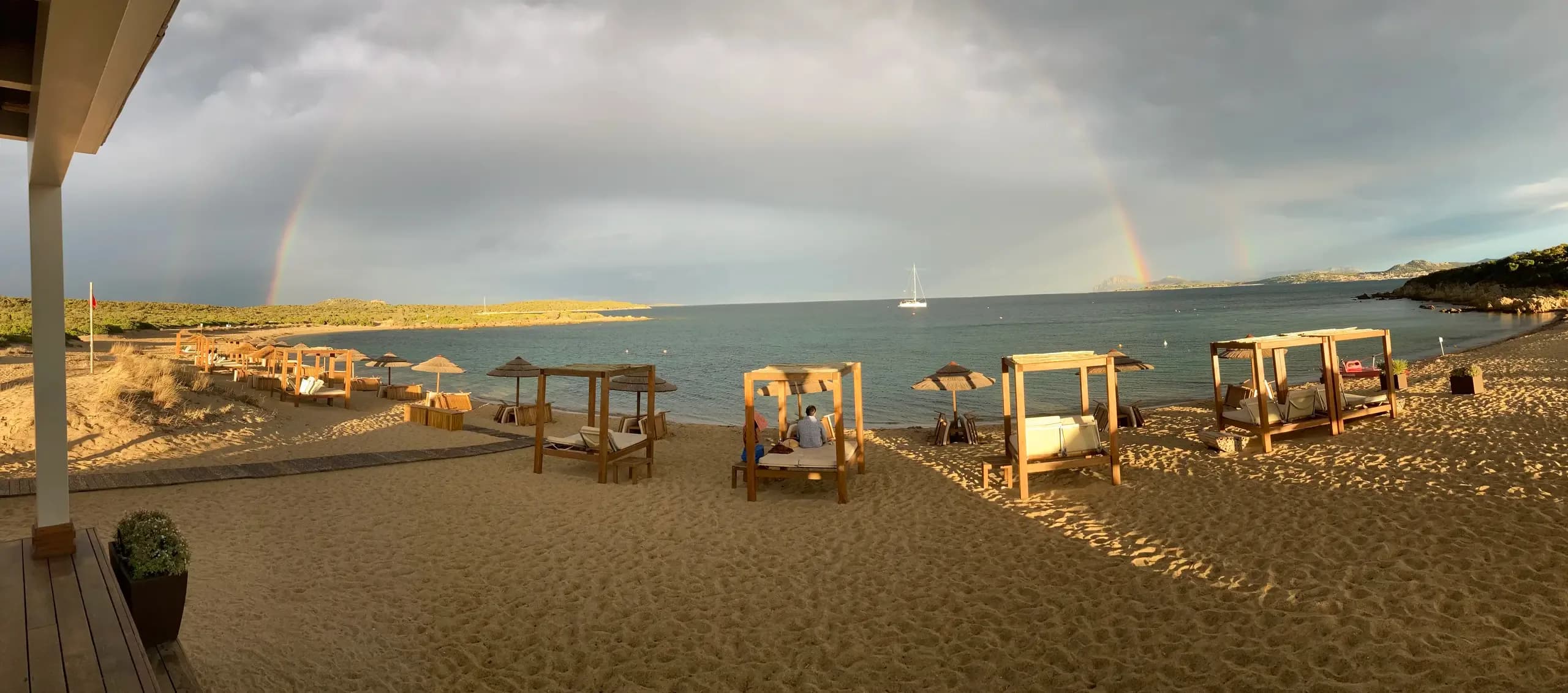Regenbogen über Strandcabanas und ruhigem Meer