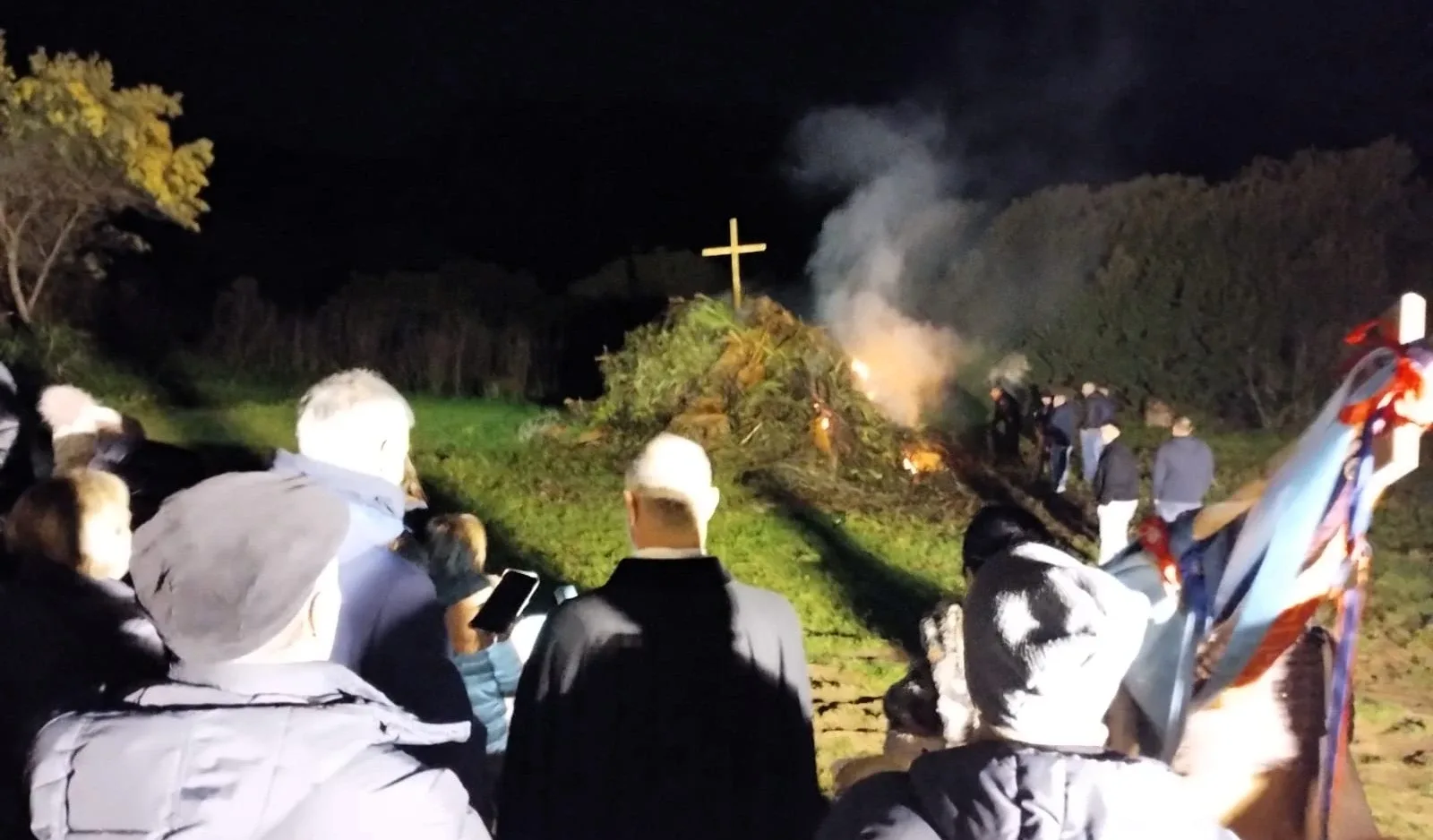 Menschen versammeln sich nachts um ein Feuer mit Kreuz.