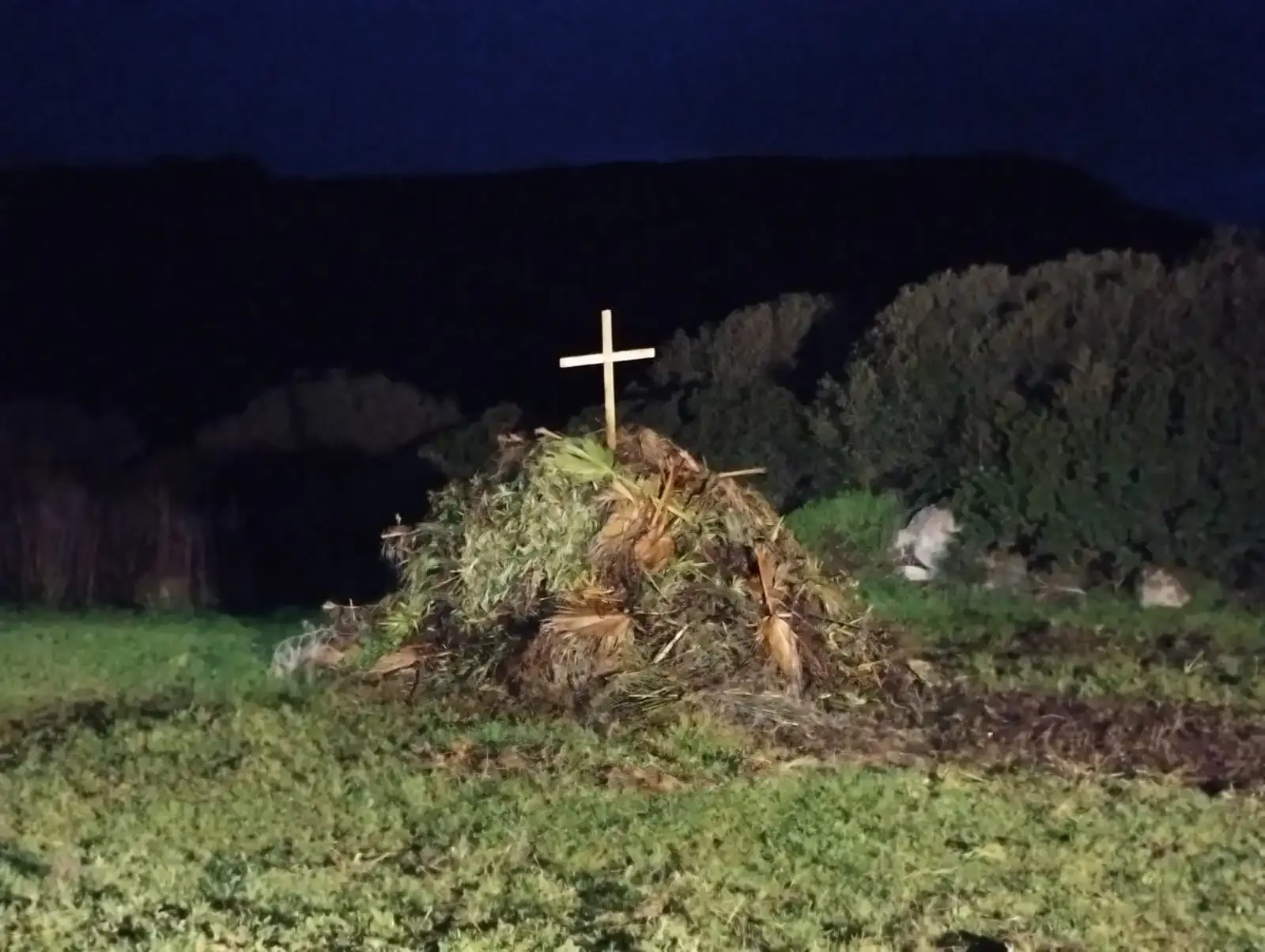 Reisighaufen mit einem Holzkreuz obenauf.