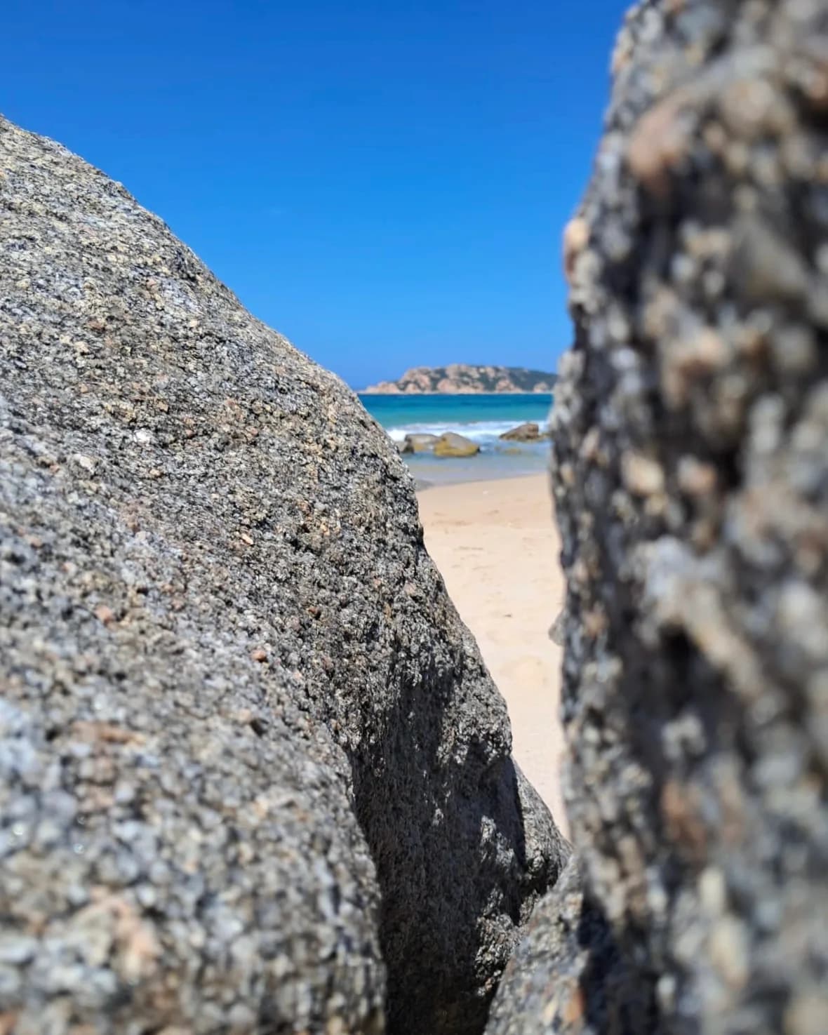 Vue de plage à travers des rochers, île au loin.