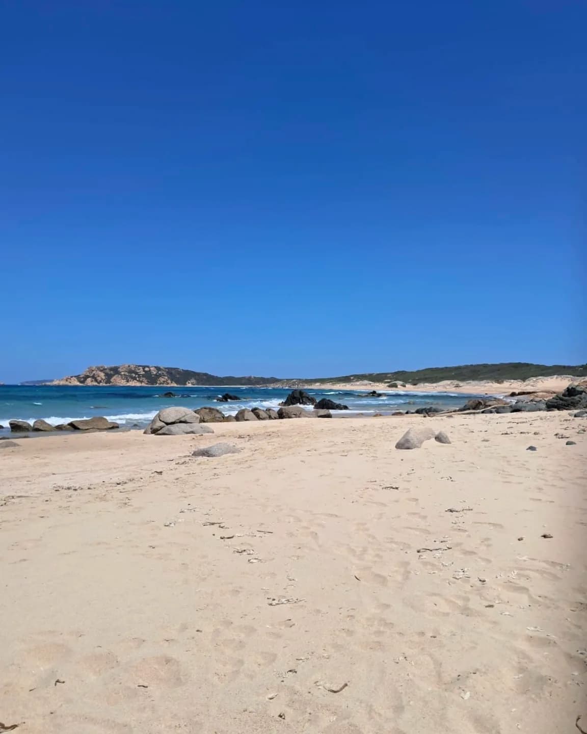 Plage de sable avec rochers sous un ciel bleu clair