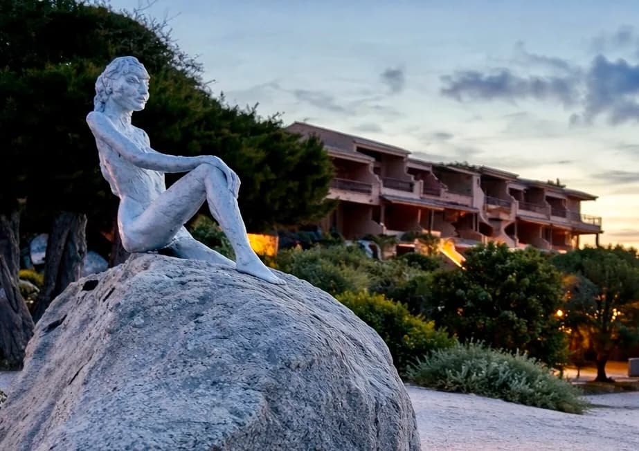 Statue on rock, resort in background, sunset.