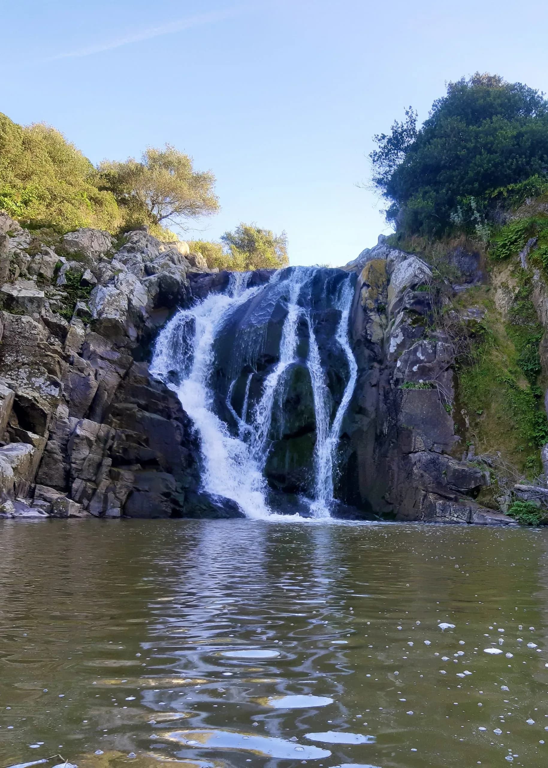 Waterfall cascading into pool, surrounded by rocks.