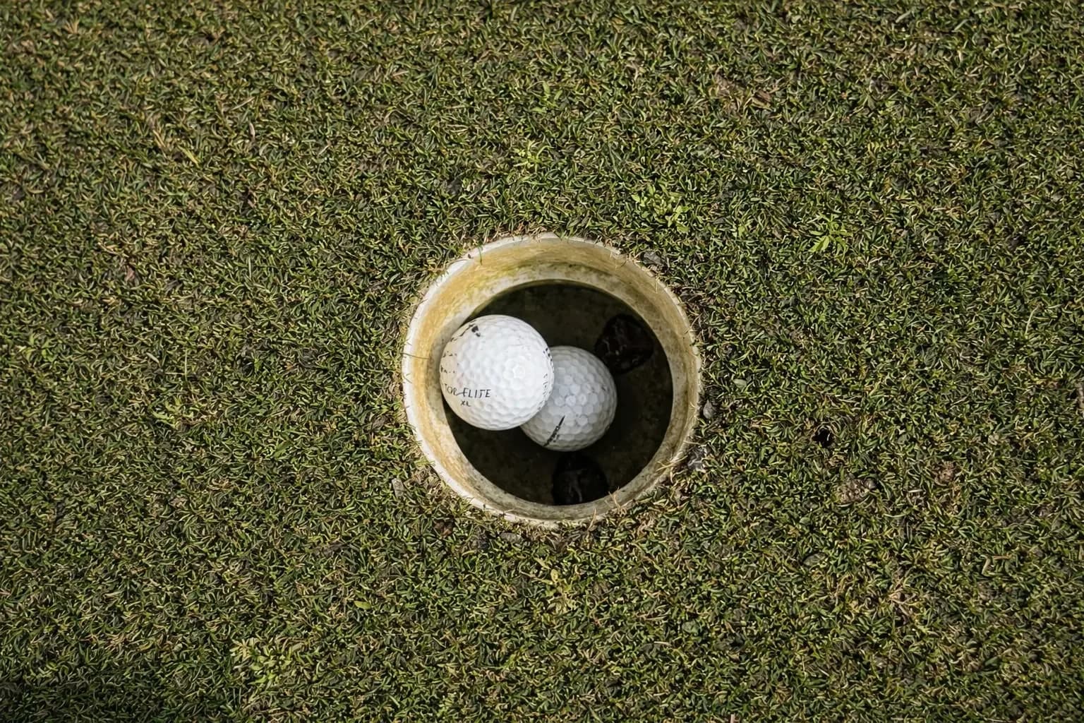 Two golf balls in the hole on green.