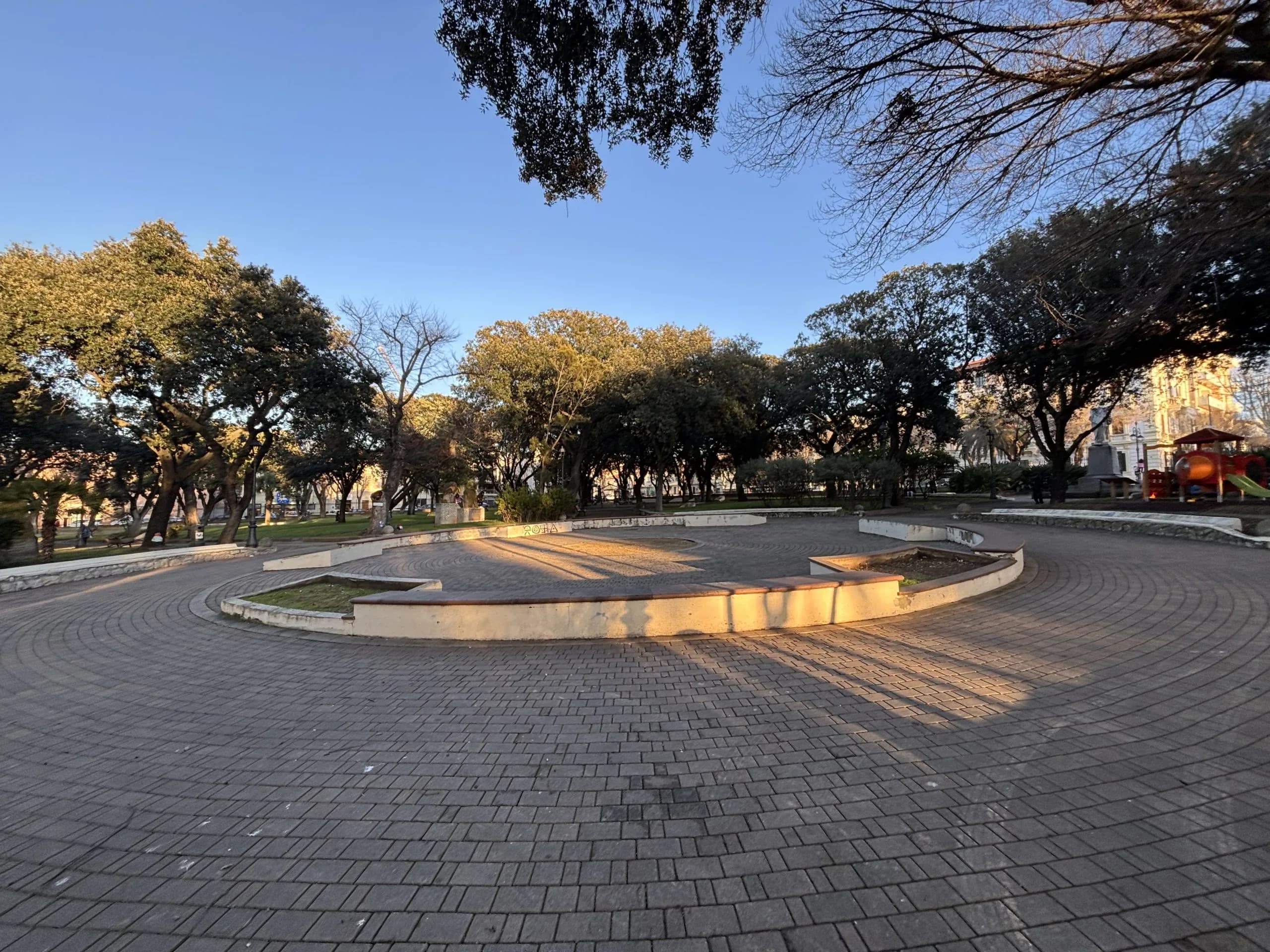Parc ensoleillé avec arbres et allée pavée.