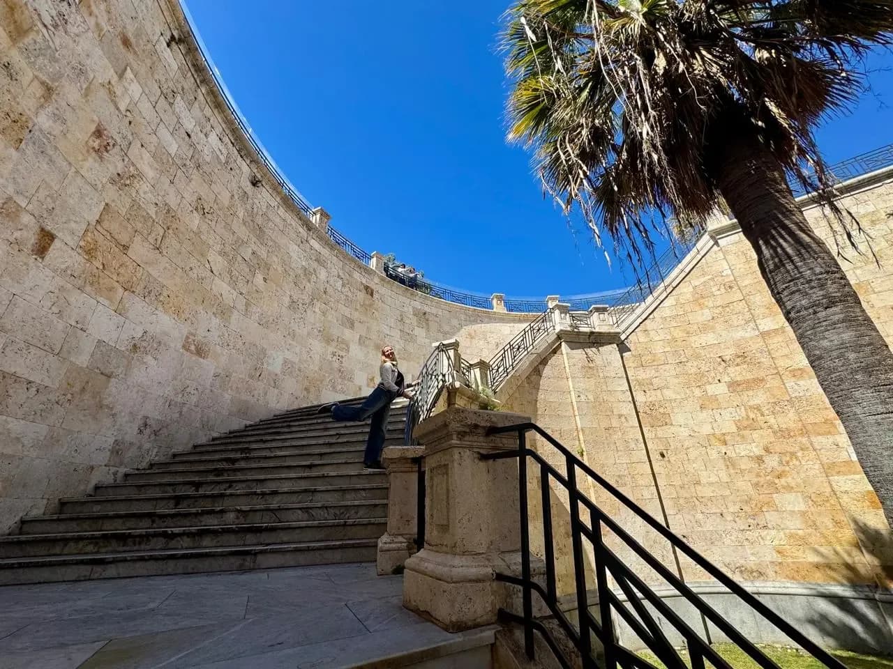 Woman poses on grand stone staircase with palm tree.
