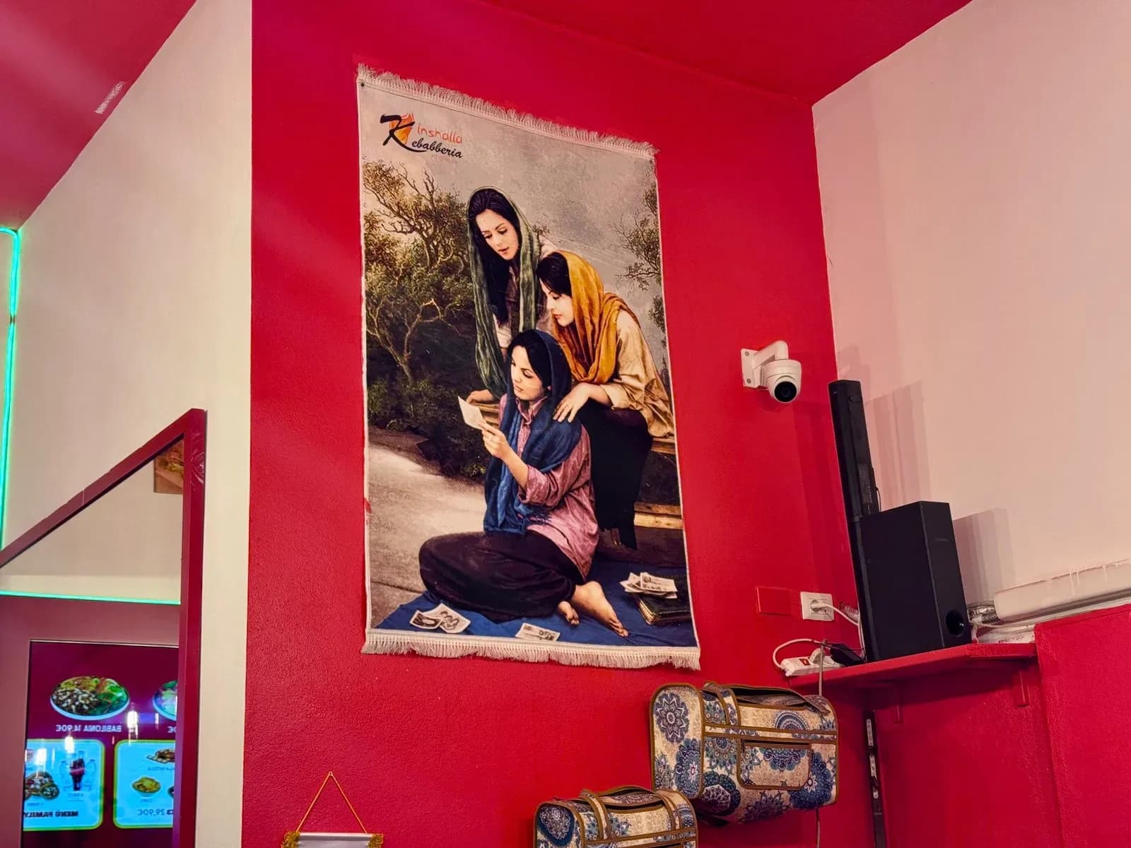 Tapestry of women reading on red restaurant wall.