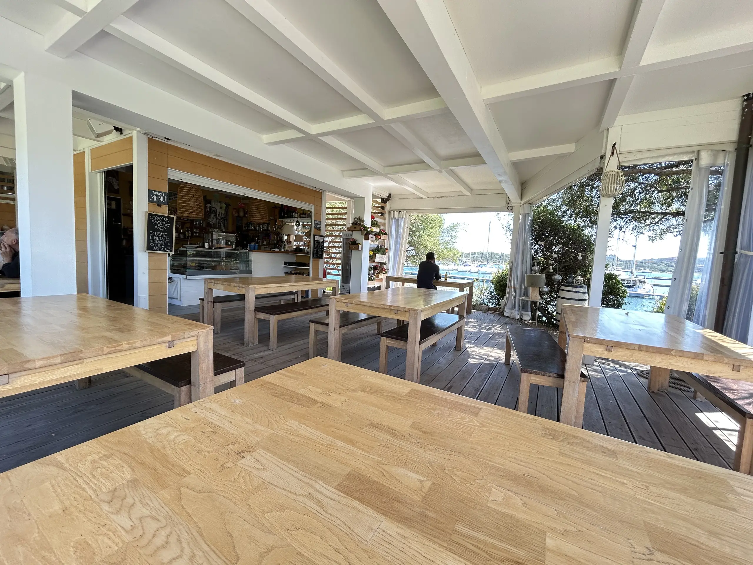 Openluchtcafé aan zee met houten tafels en uitzicht op de jachthaven
