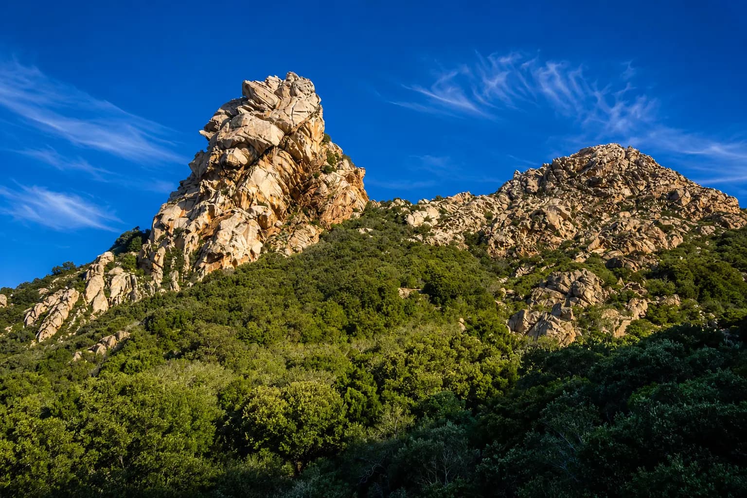 Rocky mountain formation above green forest under blue sky