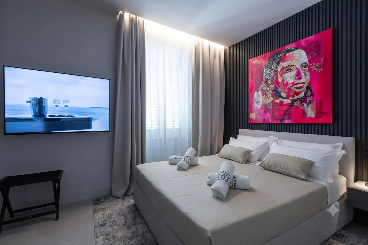Camera da letto moderna presso AZULIS Delle Terme Suites a Olbia con letto bianco, cuscini floreali, asciugamani arrotolati, TV a schermo piatto, vivace ritratto pop art e tende a tutta altezza con vista sul giardino