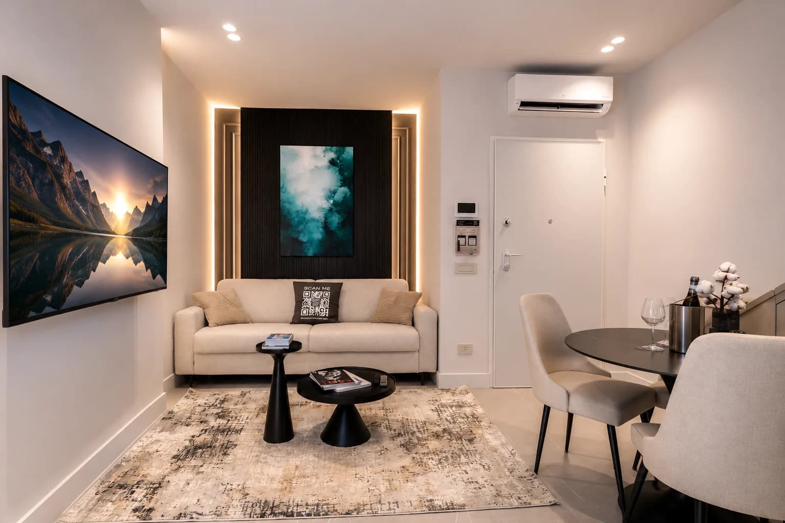Soggiorno moderno presso AZULIS DelleTerme Suites con divano color crema, tavolini d'appoggio neri, opere d'arte con paesaggi alle pareti, illuminazione d'atmosfera e zona pranzo con tavolo apparecchiato visibile a destra