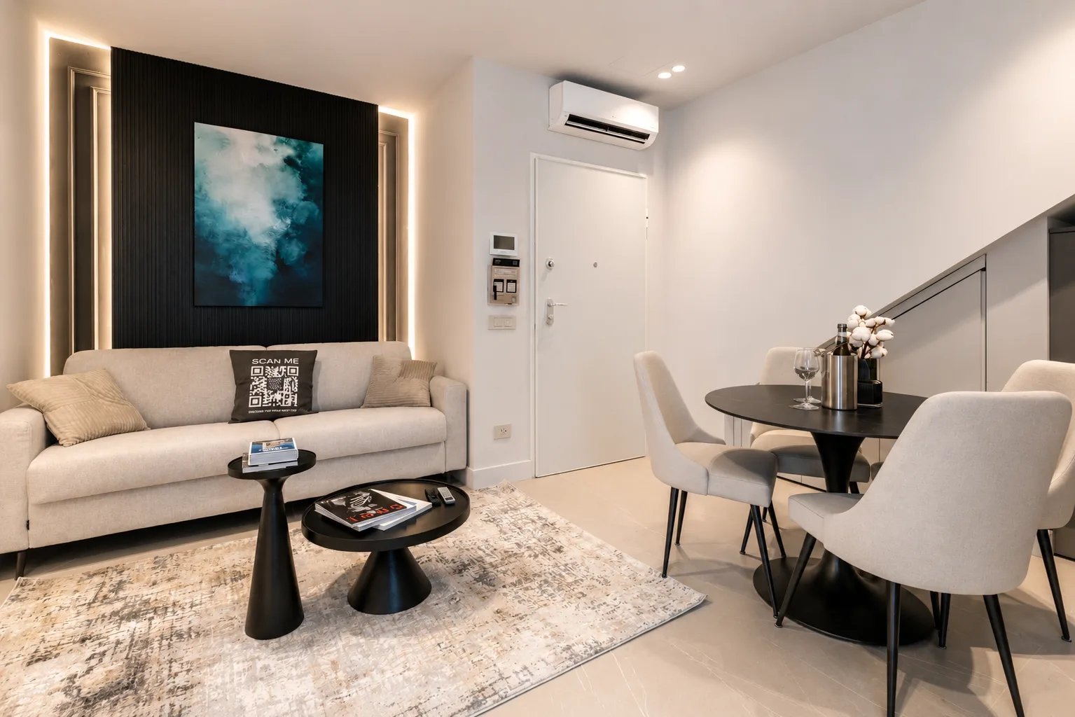 Soggiorno moderno nell'appartamento con giardino AZULIS Terme Suite, Olbia, con divano color crema, parete d'accento nera con opera d'arte turchese, zona pranzo con tavolo a piedistallo nero e arredi contemporanei