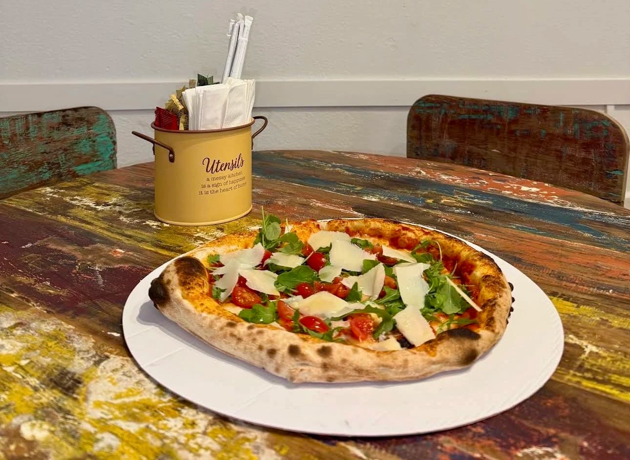 Pizza con rucola e pomodoro su tavolo rustico in legno