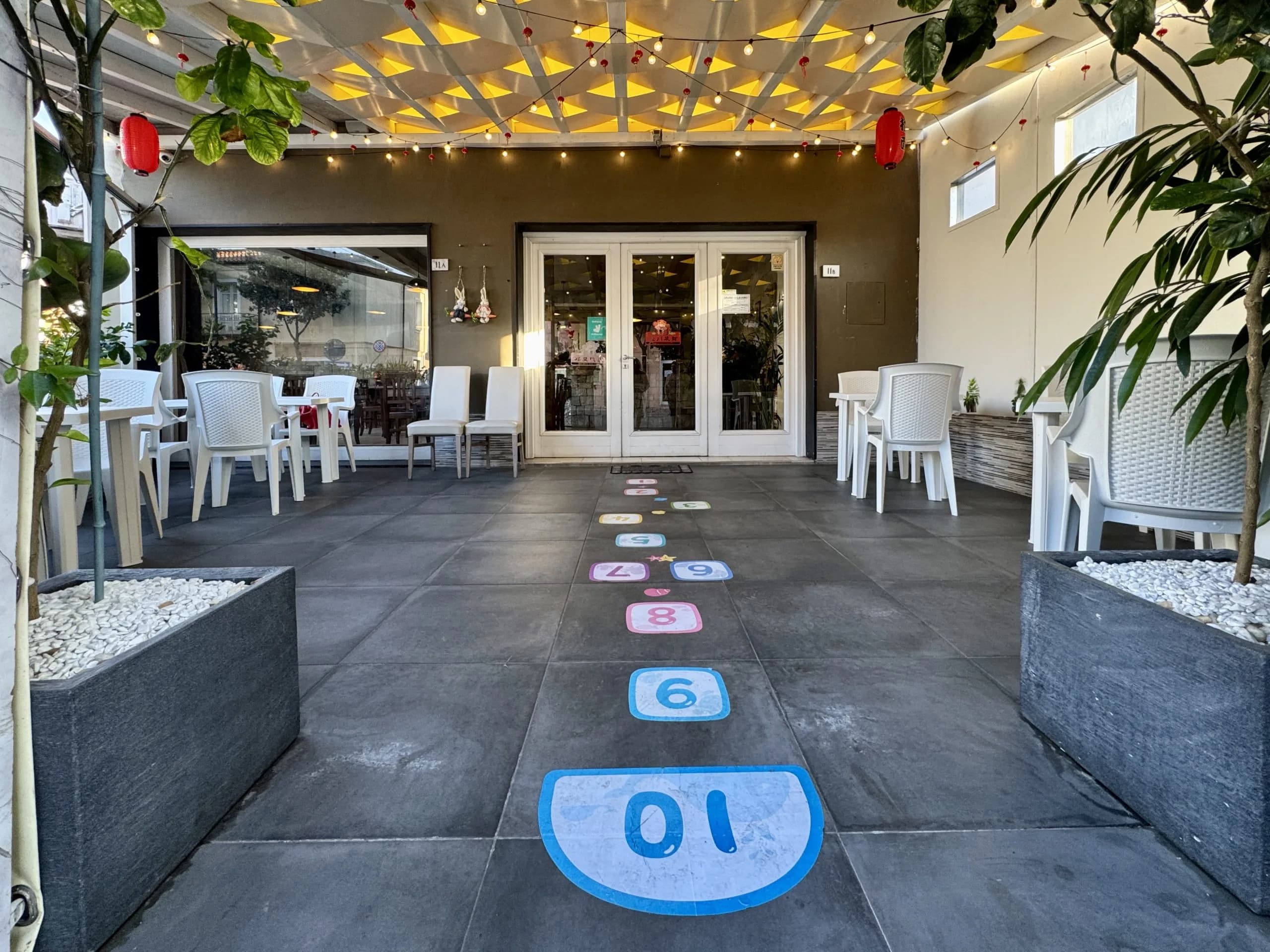 Outdoor-Café-Terrasse mit Himmel-und-Hölle-Bodenmuster und Lichterketten
