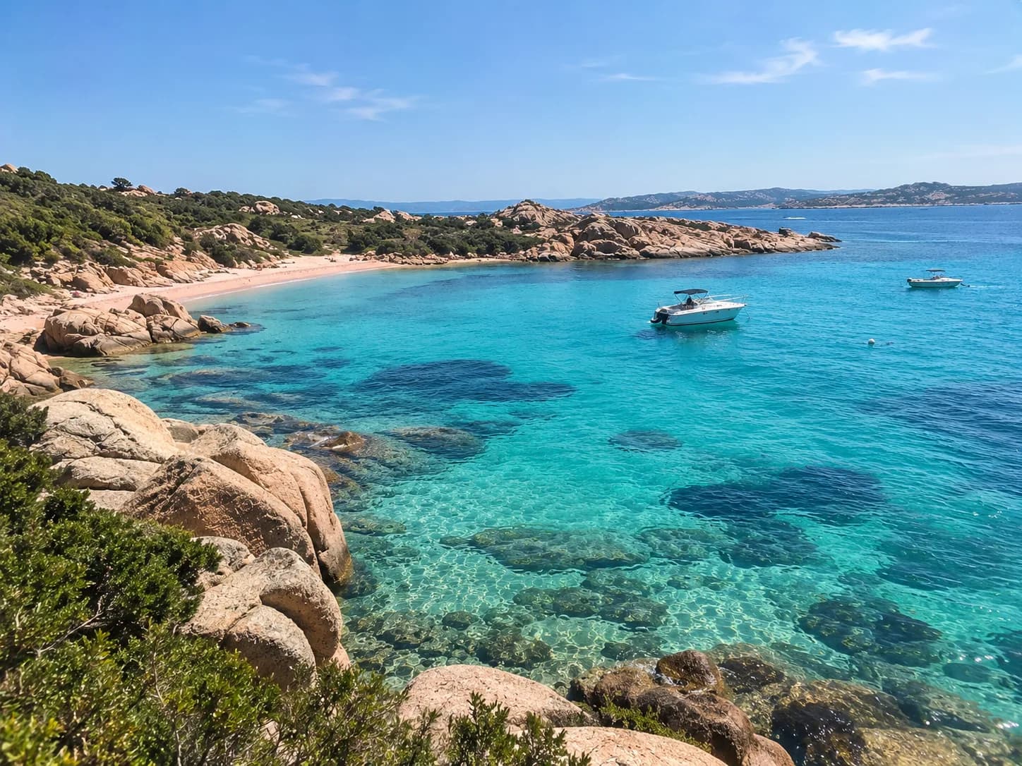 Turquoise cove with granite boulders and small boats anchored off a sandy beach in the Maddalena archipelago, Sardinia