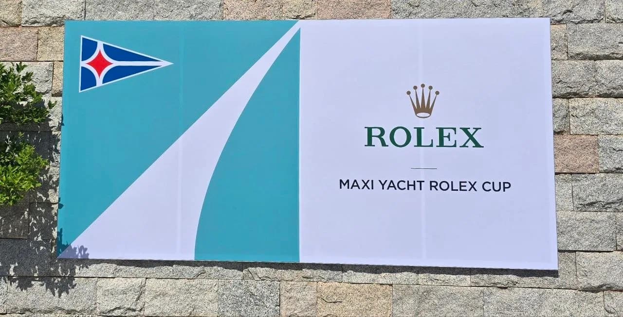 Maxi Yacht Rolex Cup banner with yacht club pennant and Rolex crown logo mounted on a stone wall in Porto Cervo, Sardinia