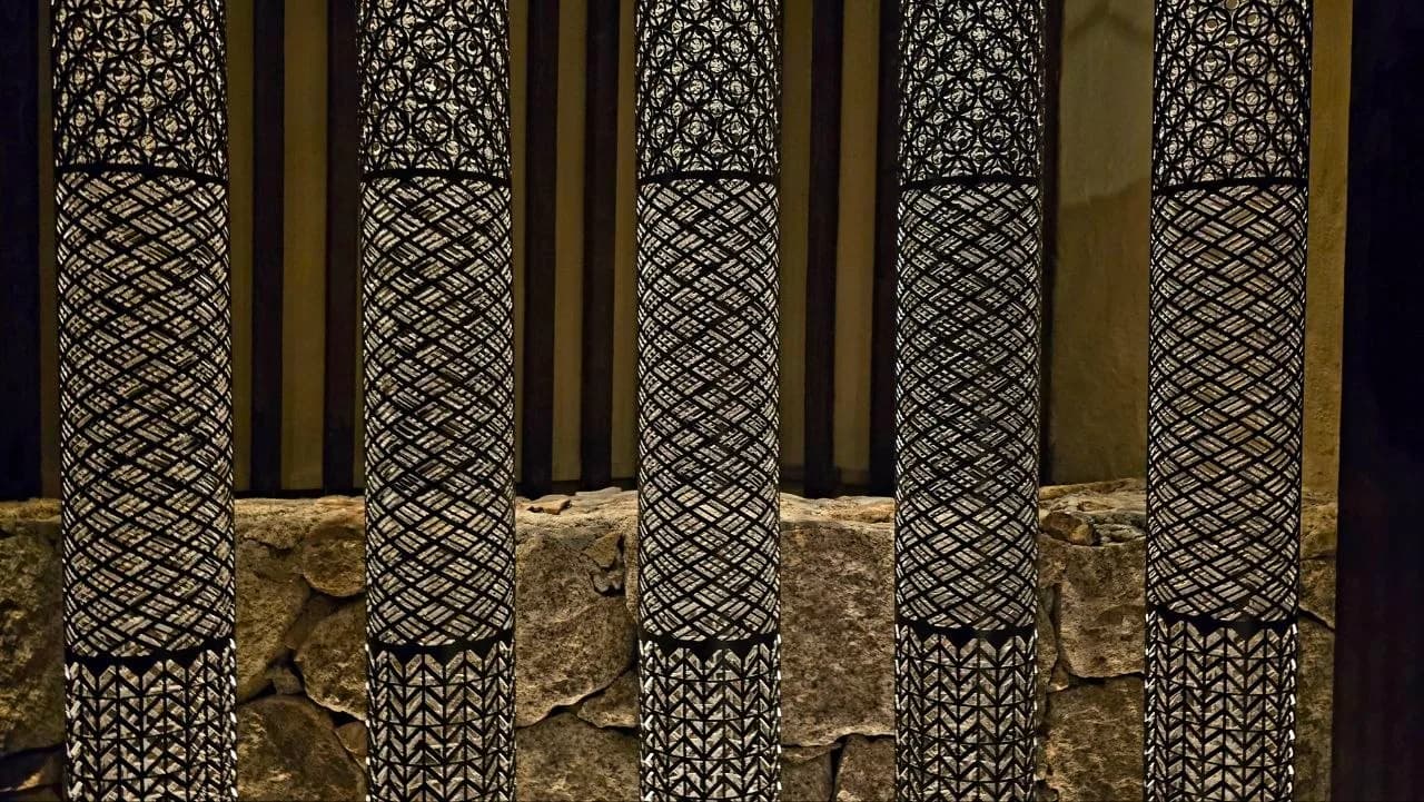 Backlit lattice-patterned columns set against a stone wall, part of Zuma Porto Cervo's decorative interior lighting.