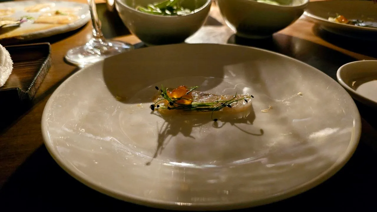 A minimalist sashimi dish topped with roe, chives and sesame seeds on a large ceramic plate, part of a Japanese tasting menu at Zuma Porto Cervo.