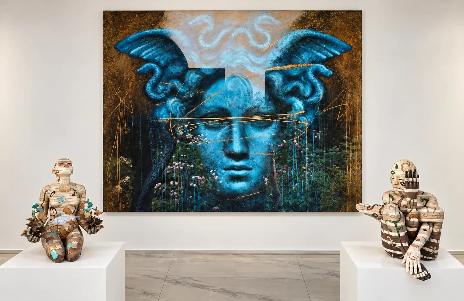 Large painting of a blue Medusa face flanked by two painted figure sculptures on white plinths