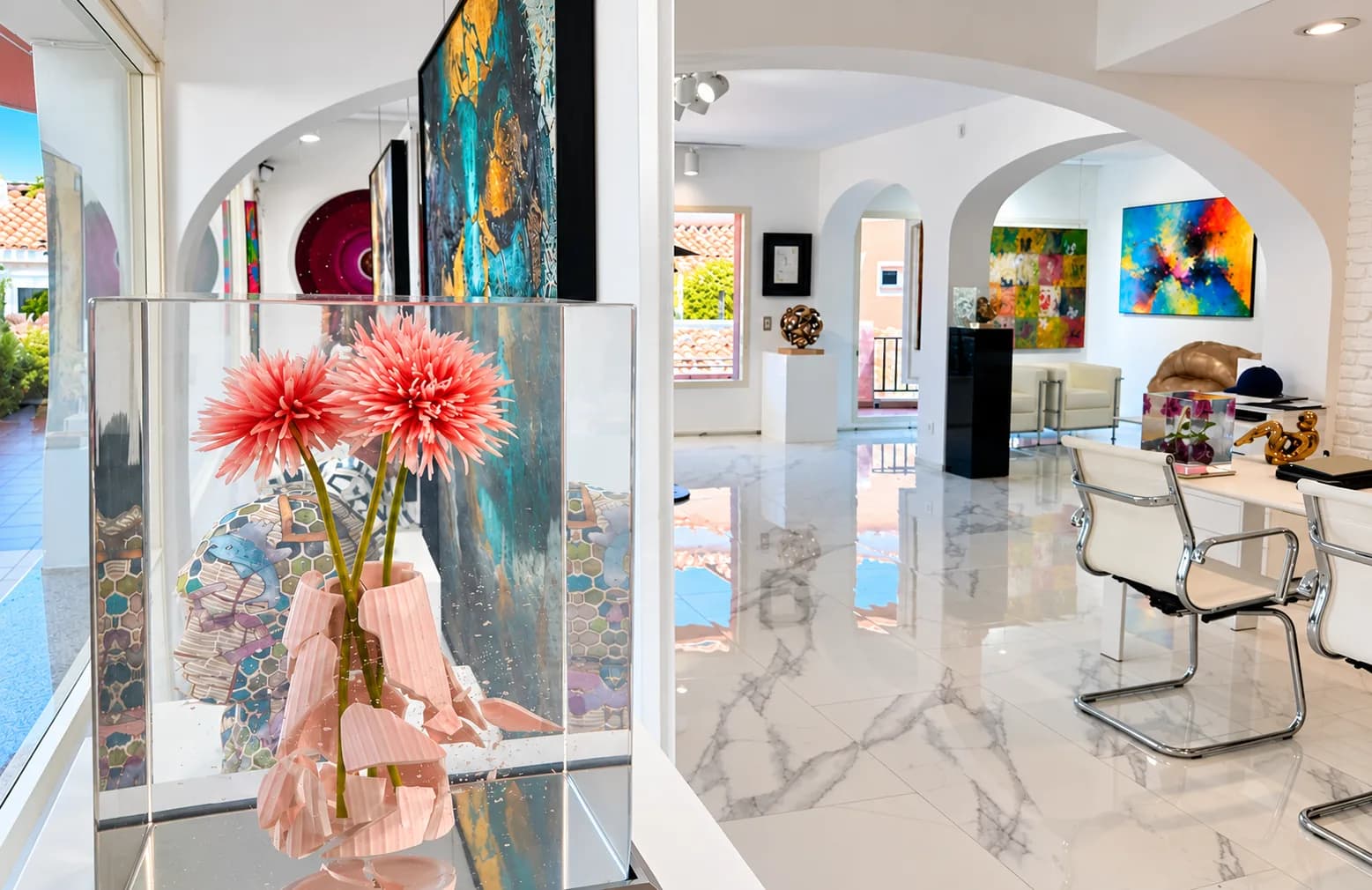 Bright gallery interior with marble floor, arched rooms, colourful abstract paintings and a glass case with flowers