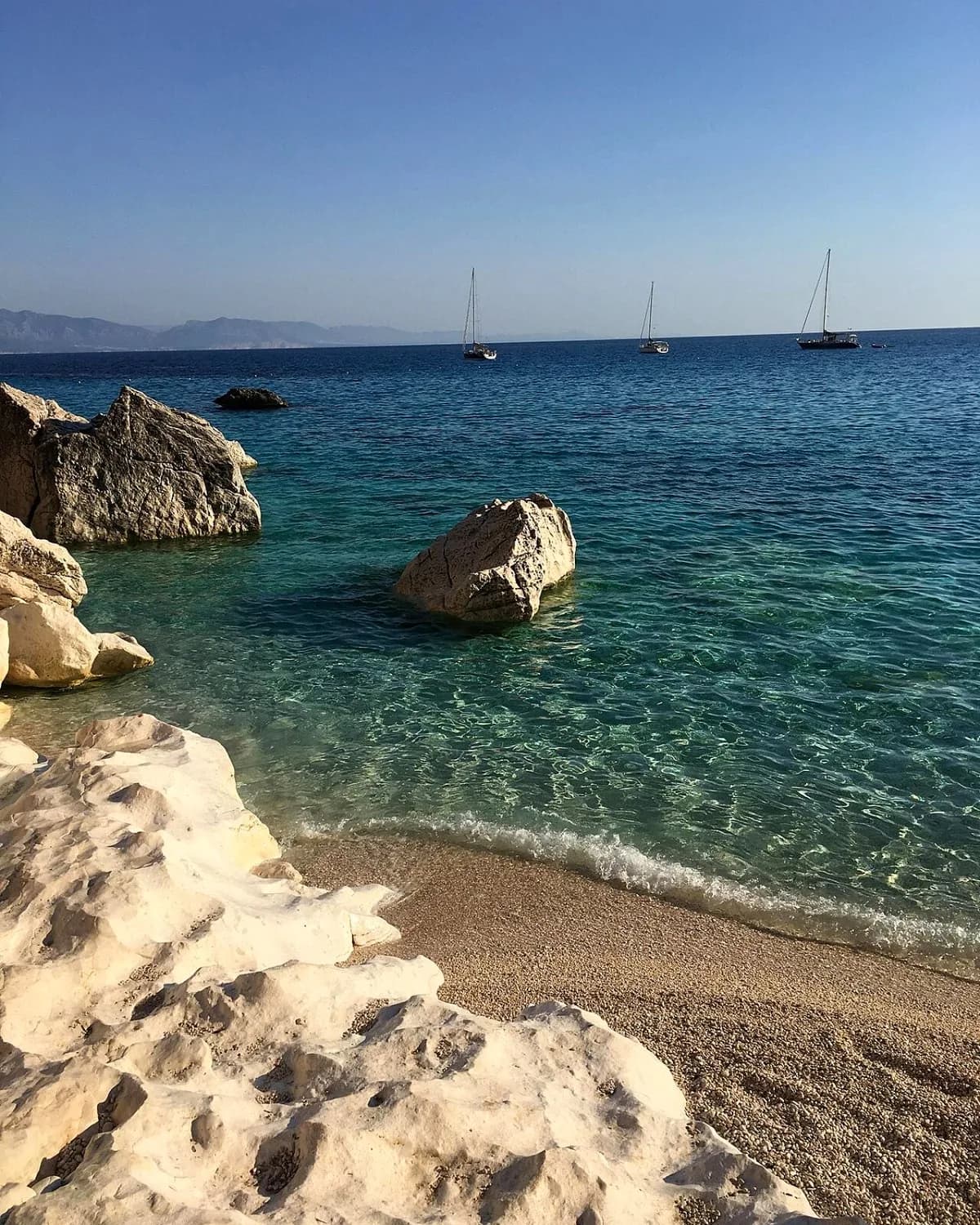 White limestone rocks and clear turquoise water at Cala Goloritzé, with three sailing boats anchored offshore