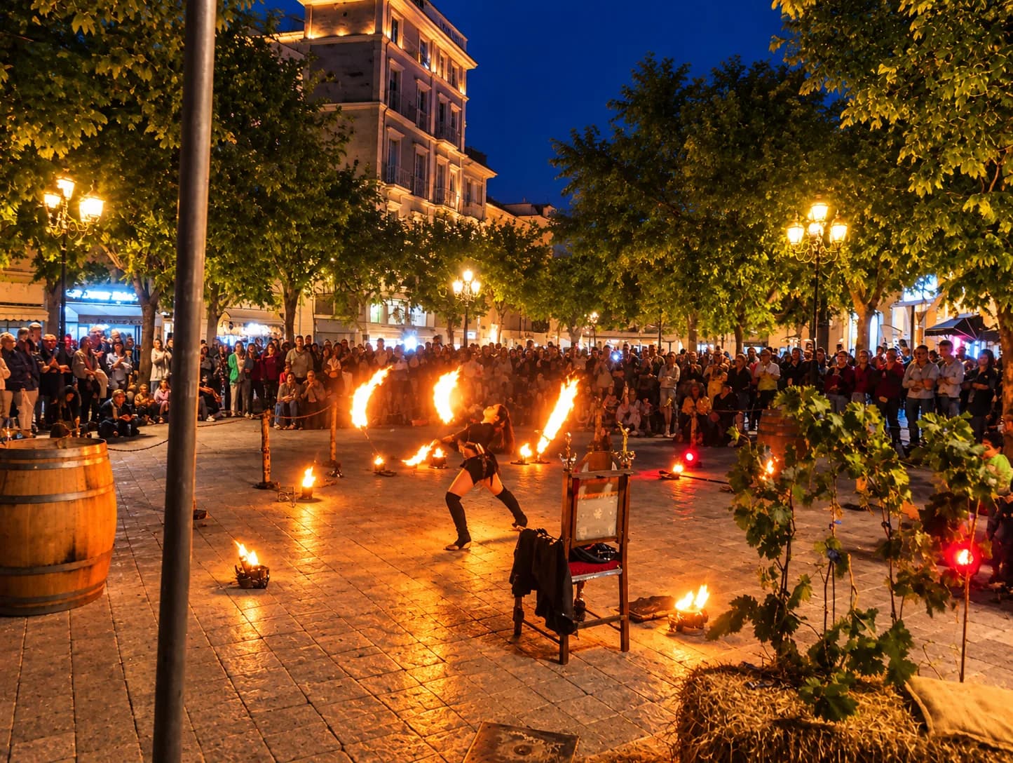 Avondmenigte op een plein in Olbia met kaarslantaarns op palen, verlichte historische gebouwen en een wijnvat voor een winkelpui.
