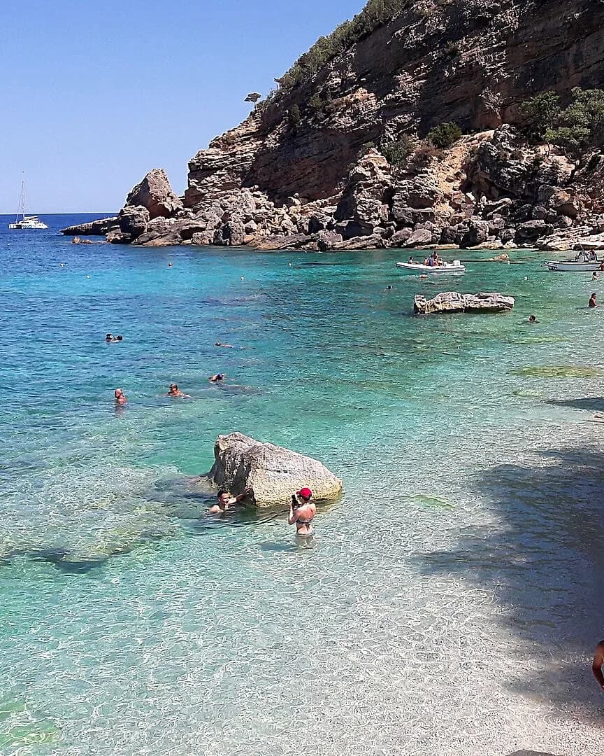 Turquoise shallow water at Cala Mariolu, Sardinia, with distant swimmers, a line of buoys and boats offshore