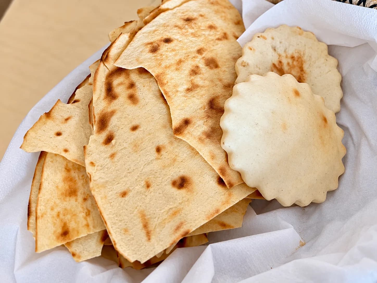Corbeille tapissée de papier blanc contenant des feuilles de pain plat fines et croustillantes aux taches brunes grillées, à côté de deux pains ronds moelleux aux bords festonnés.