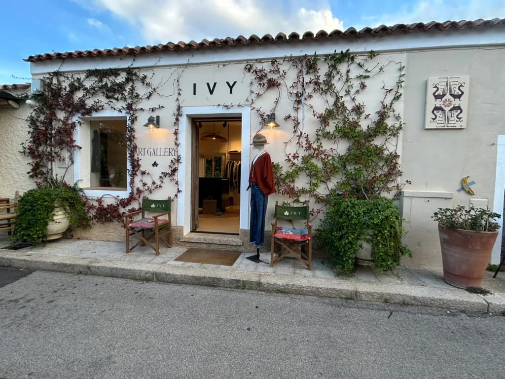 Whitewashed boutique in San Pantaleo named Ivy, its facade covered in climbing vines, with a dressed mannequin, folding chairs and terracotta plant pots outside the open doorway.