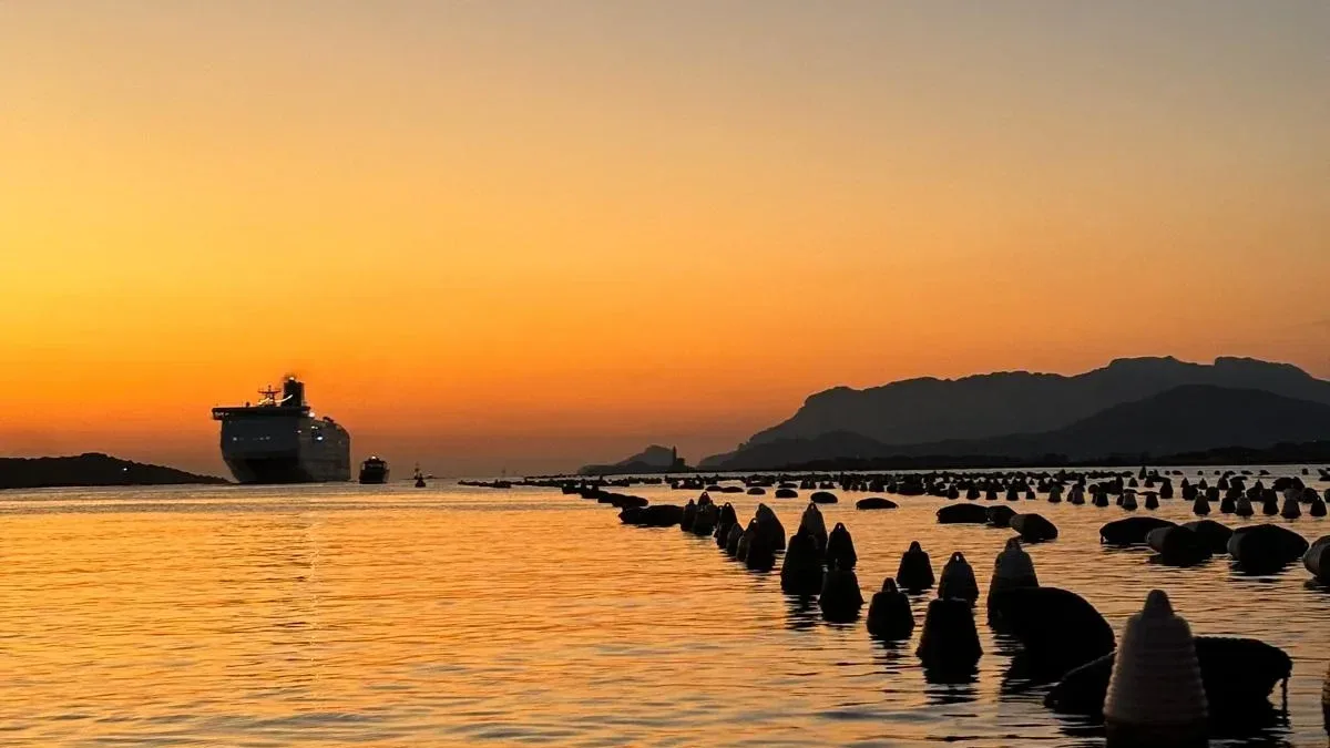 Ferry on the Gulf of Olbia at sunset behind rows of oyster-farm buoys, with mountains on the horizon