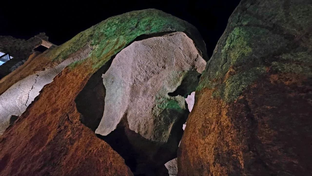 Large granite boulders lit in orange, green and white against the night sky