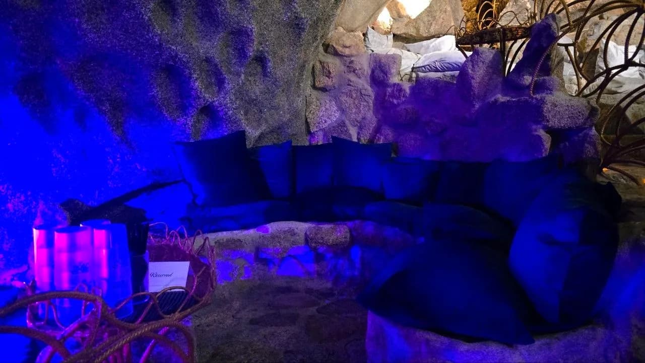 Reserved lounge area with cushioned stone seating set into a granite rock wall, lit in blue
