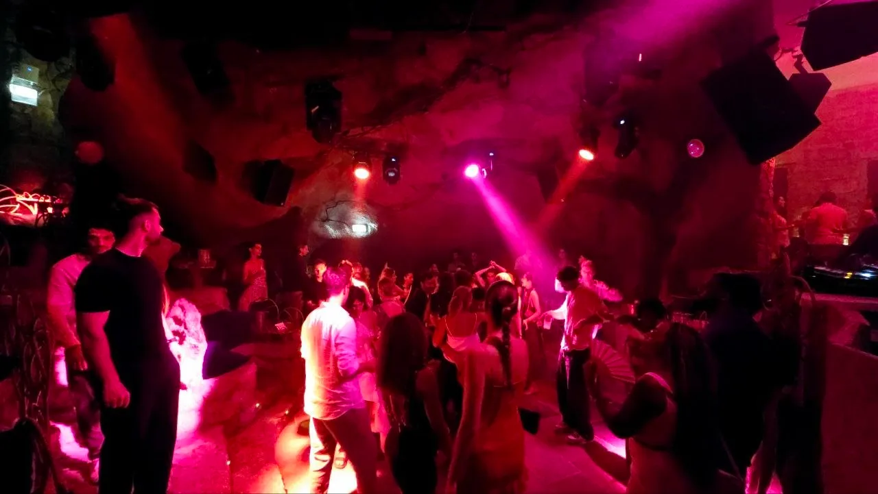 Crowd dancing under pink and red stage lights inside Ritual Club's rock-walled dance floor
