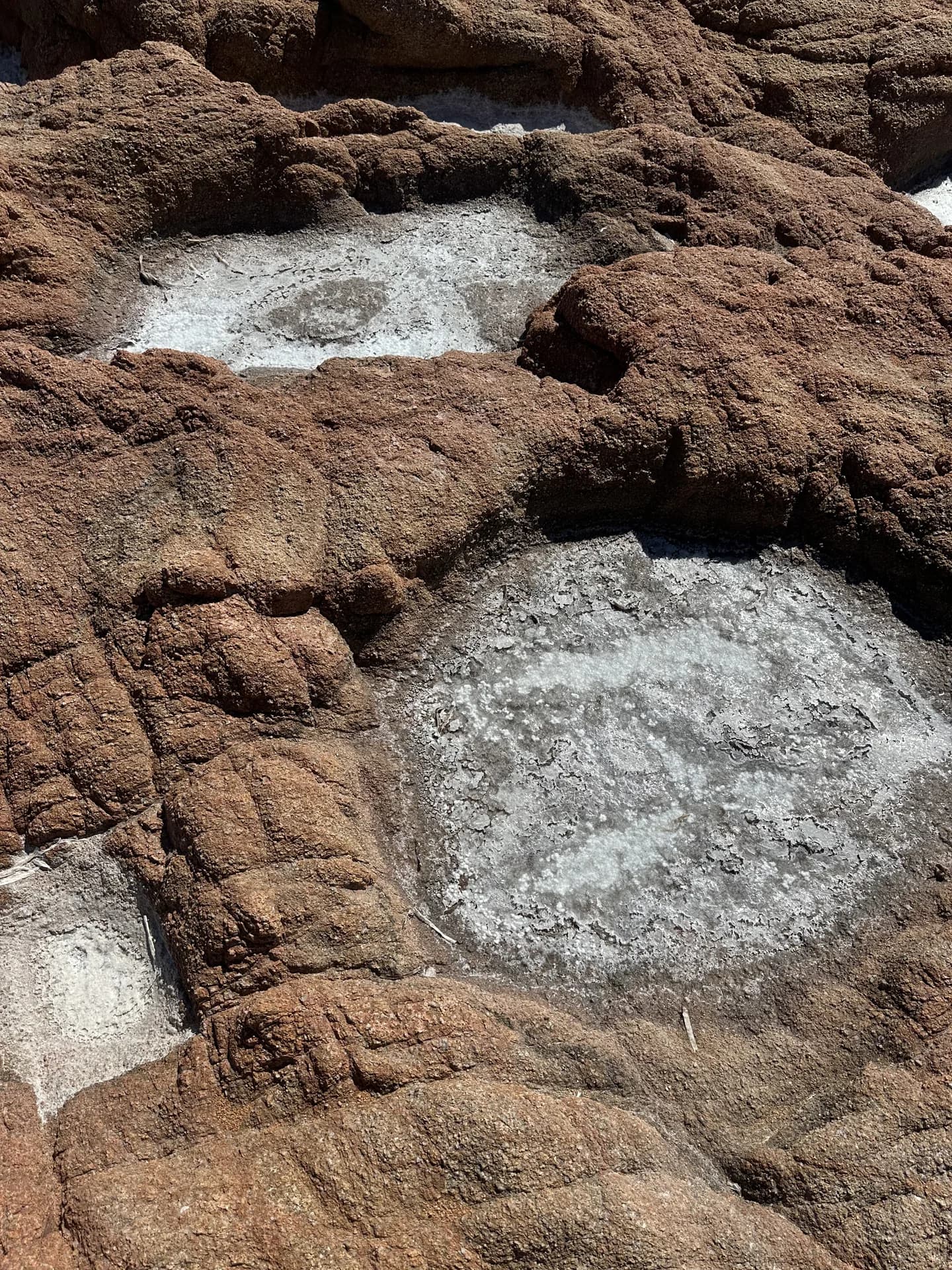 Close-up of weathered reddish-brown granite boulderPockets of dried white salt crystals in rock hollows along the beach by via Cappaccia