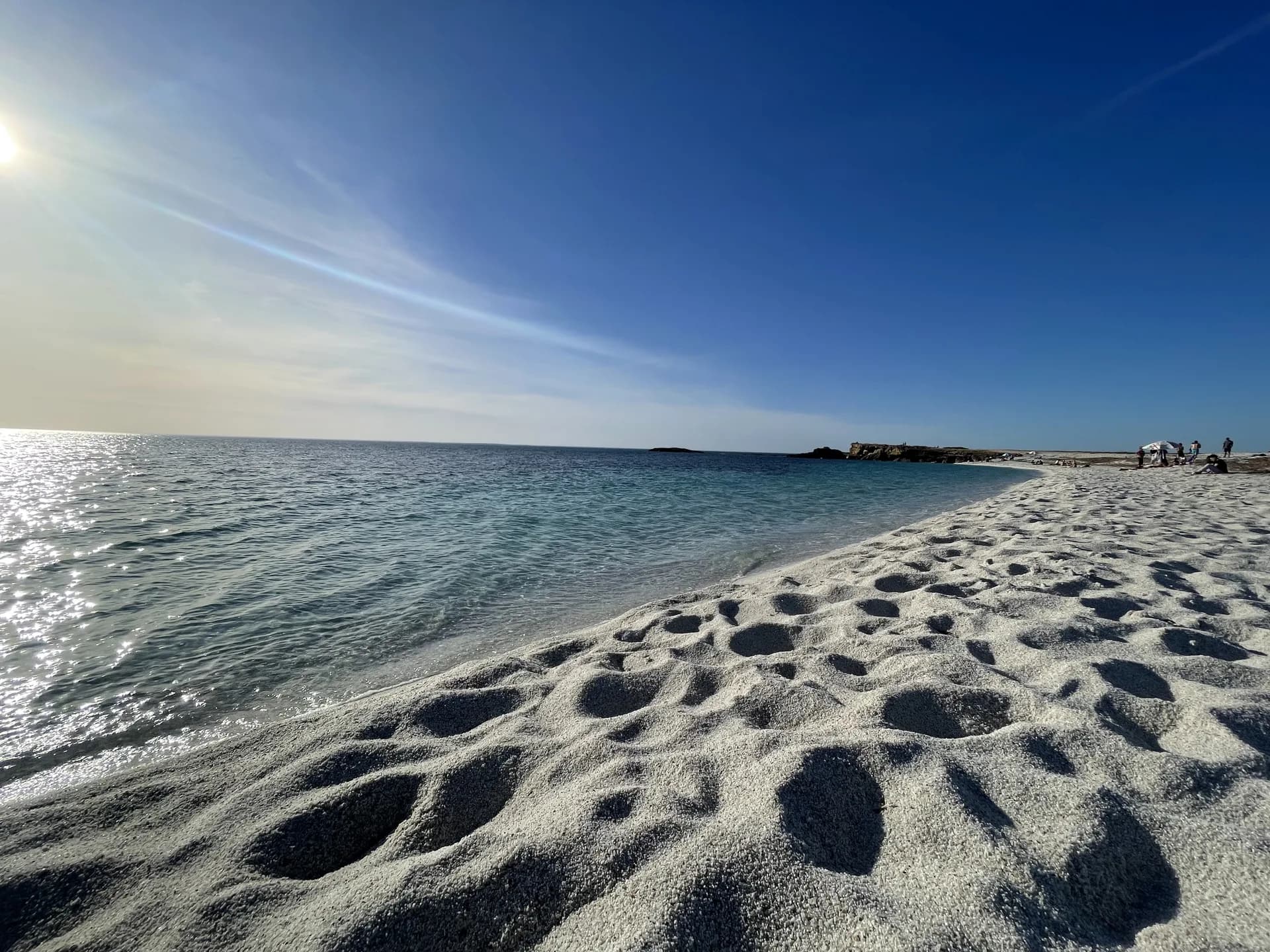 Footprints in the pale quartz grains of Is Arutas beach as the sun sits low over the sea