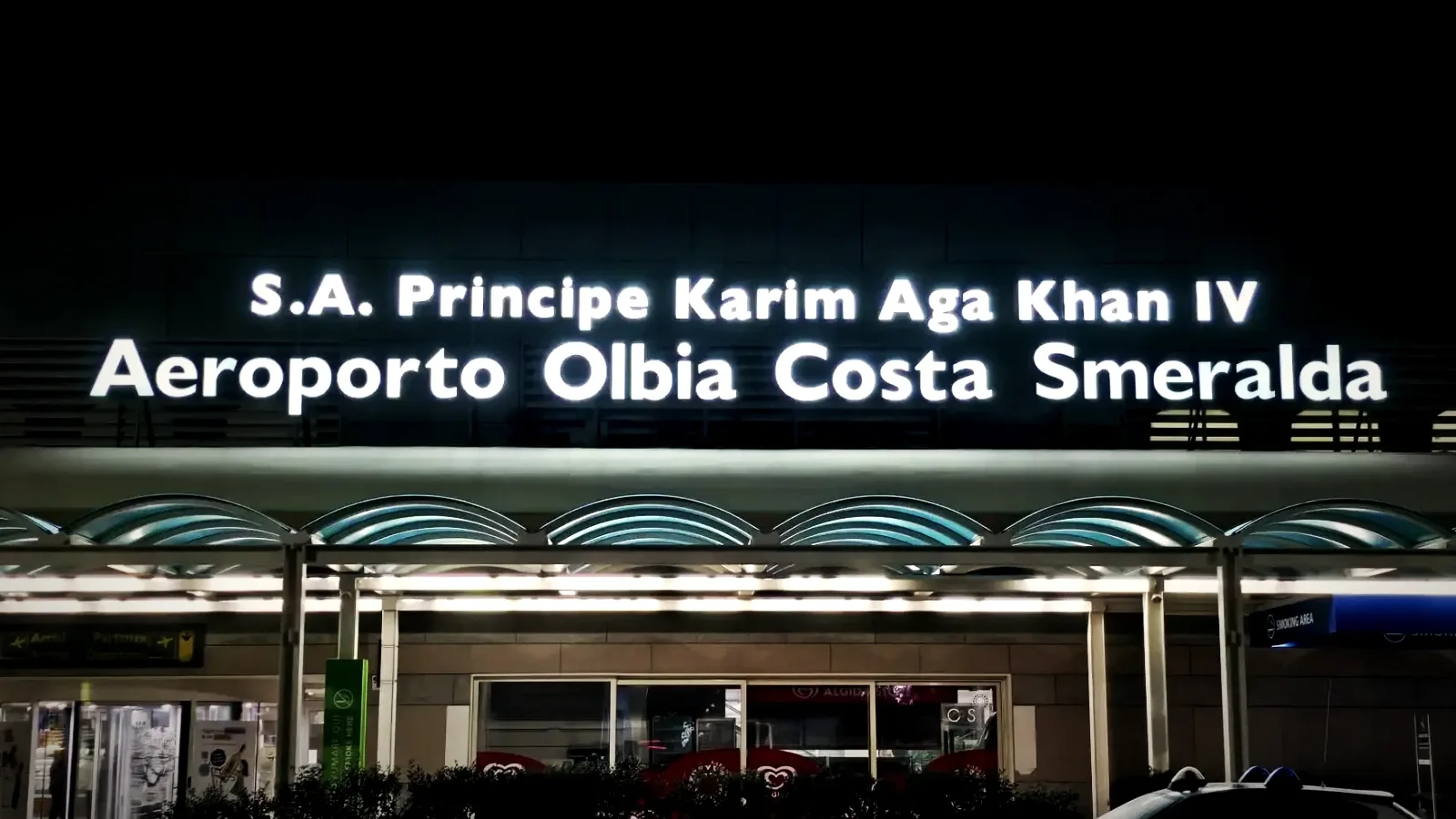 The terminal of Olbia Costa Smeralda airport at night, its illuminated sign above the entrance, Gallura, Sardinia