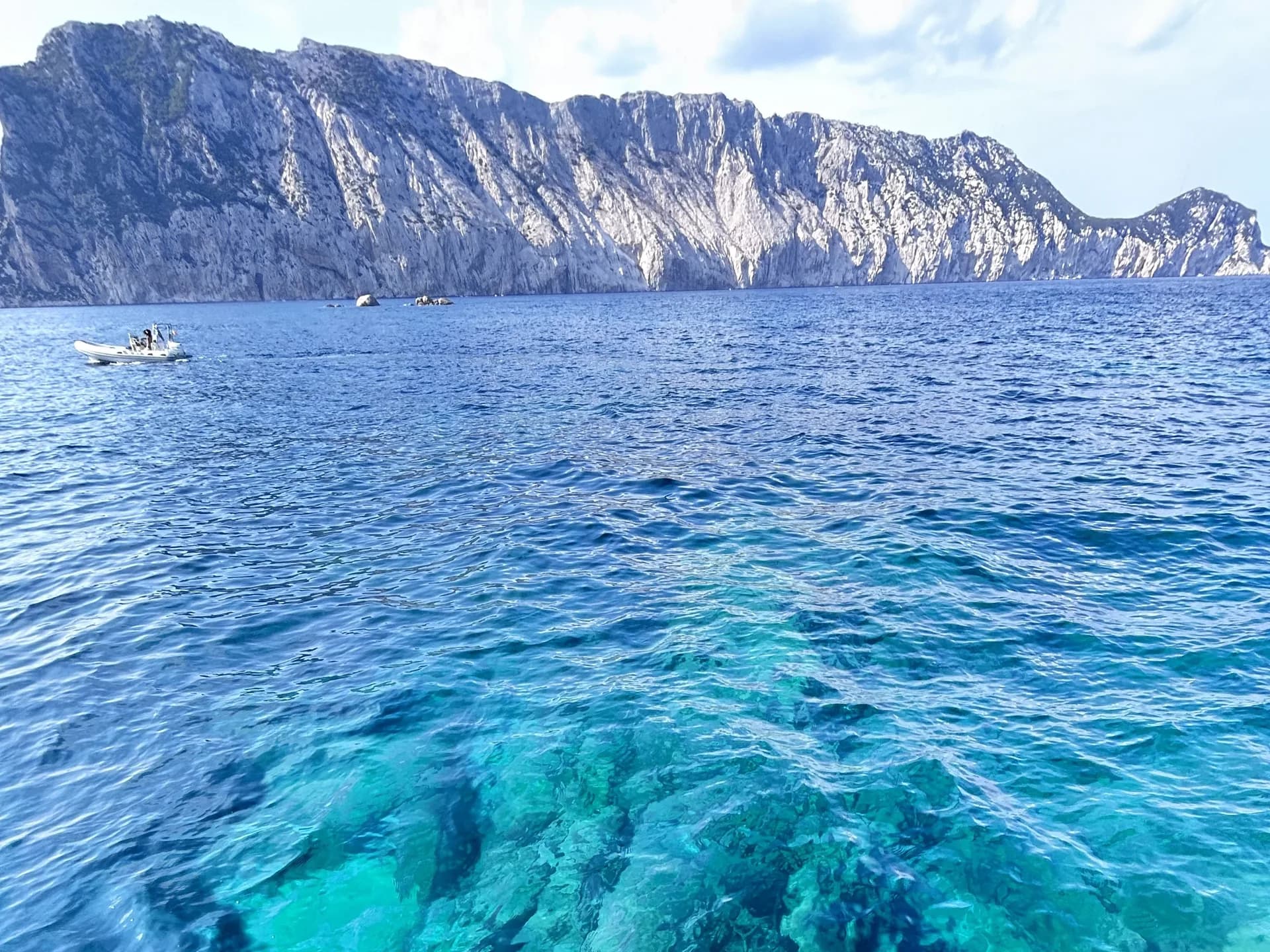 Mer turquoise limpide avec un petit bateau à moteur sous les falaises calcaires imposantes de l'île de Tavolara, près d'Olbia, en Sardaigne
