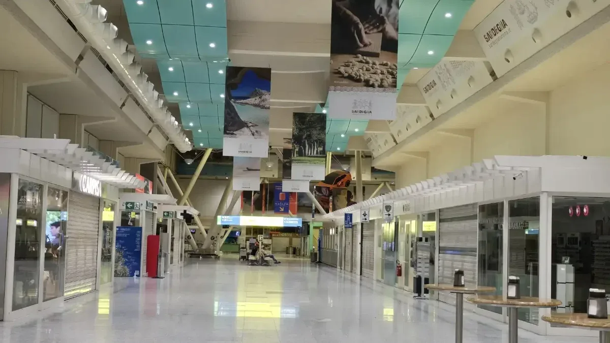 Empty departure hall at Olbia Costa Smeralda airport out of season, with shuttered shops and high tables along a polished floor