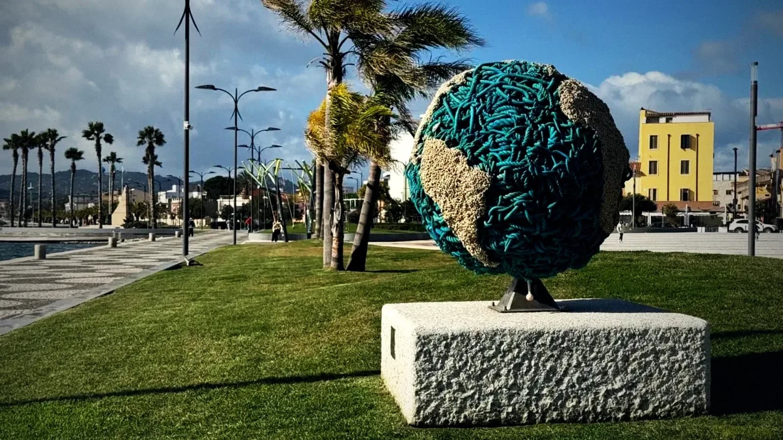 Globe sculpture on the Olbia waterfront promenade, with palm trees and the town behind, Gallura, Sardinia