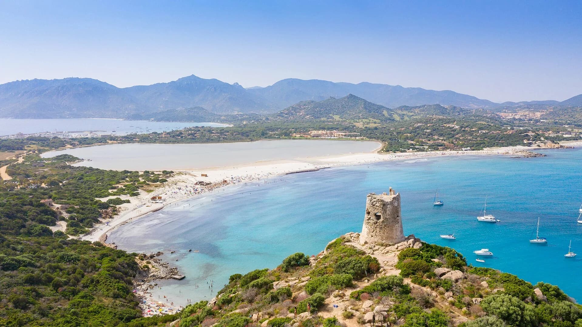Aerial view of Porto Giunco beach in Villasimius, Sardinia, with the Torre di Porto Giunco watchtower and the Stagno di Notteri pond behind the beach